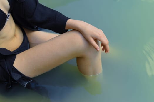 Part of the body, leg and arm of a young woman in a dark dress sitting in the water. Selective focus