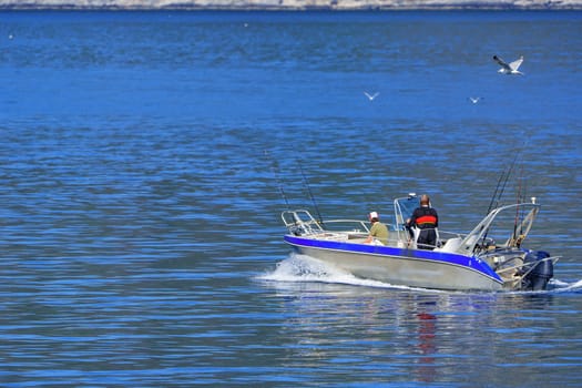 Fishermen on an aluminum boat, navigating the Norwegian Sea with crystal-clear waters and stunning mountains in the background, creating a picturesque scene of exploration and adventure.