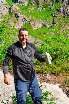 A tourist is refreshing himself by pouring cold water over his head in the mountain wilderness on a hot sunny day, taking a break from the heat and enjoying the natural surroundings.