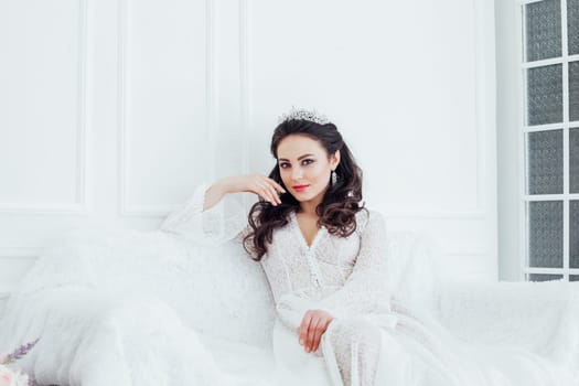 the bride in a wedding dress with a Crown sitting on a white sofa in a room