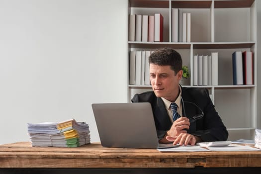 Unhappy young businessman feeling bored and stressed at work looking at laptop with hopeless expression while sitting in office.