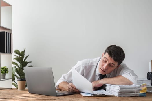 Unhappy young office worker feeling bored at work looking at laptop with a hopeless expression while sitting in the office. Male office worker feeling tired from monotonous work..