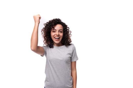 pretty confident positive young caucasian woman with black curly hair is dressed in a gray t-shirt on a white background with copy space.