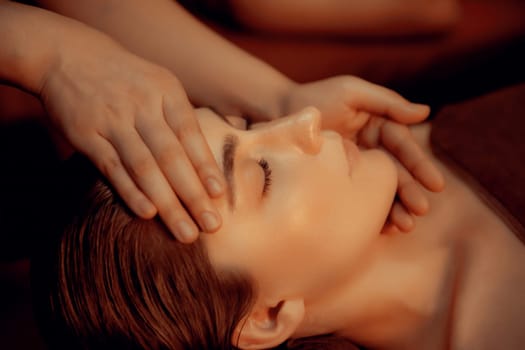 Closeup caucasian woman enjoying relaxing anti-stress head massage and pampering facial beauty skin recreation leisure in warm candle lighting ambient salon spa in luxury resort or hotel. Quiescent
