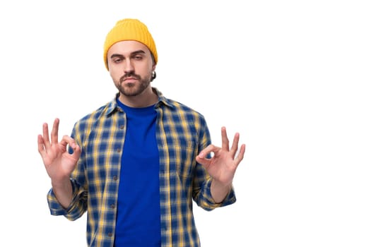 young stylish brunette man with a beard and mustache in a shirt and hat thinks holding his head.