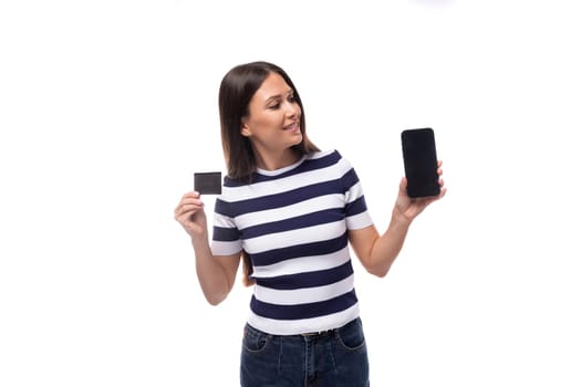 young smart brunette european lady of slim build dressed in black and white t-shirt offers advertising on smartphone holding credit card mockup.