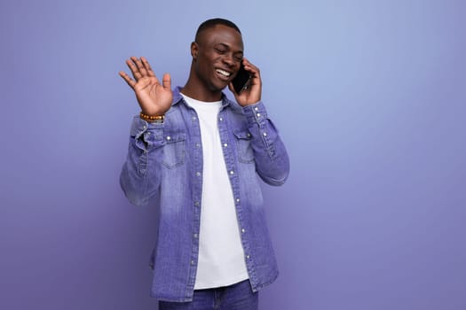 portrait of a well-groomed emotional young attractive african man dressed casually in denim clothes chatting on the phone.