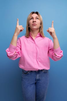 young blond caucasian woman with flowing straight hair dressed in a pink blouse and jeans pointing fingers up thoughtfully.