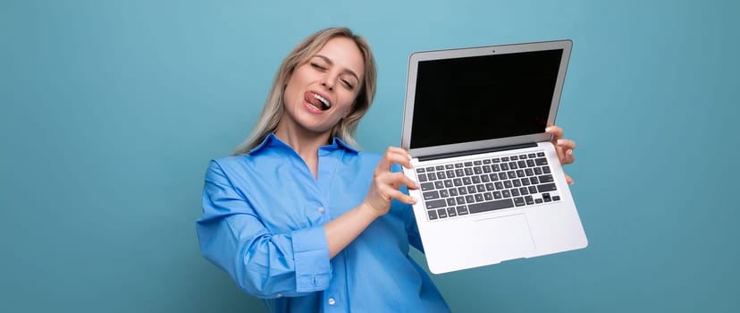 photo of adorable cute blond girl showing open laptop with empty space for website on blue background.