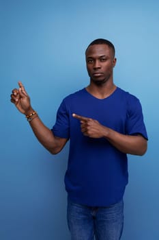 attractive 25s african guy in casual blue t-shirt pointing his finger to the side.