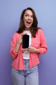 a cute brunette lady with dark hair below her shoulders in a shirt and jeans demonstrates a smartphone screen forward.