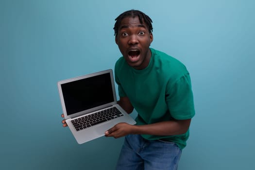 surprised joyful african young brunette male consultant in casual t-shirt with open laptop.
