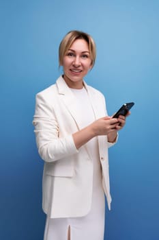 young blondie elegant female adult dressed in a jacket and dress holds a smartphone in her hands.