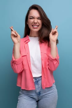 positive brunette lady with dark hair below her shoulders in a shirt and jeans crossed her fingers in anticipation of a surprise.