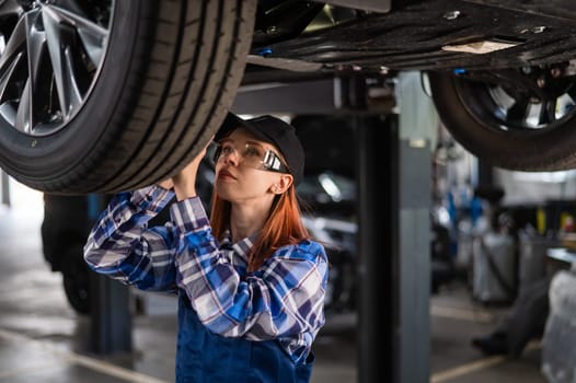 A female mechanic inspects a lifted car. A girl at a man's work