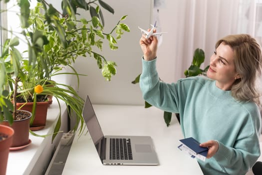 Positive happy woman going on summer holidays, sitting at office with toy plane and showing passport, having video call.