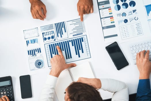 Top view analyst team utilizing BI Fintech to analyze financial data at table in meeting room. Analytic BI dashboard power on paper for business insight and strategic marketing planning. Prudent