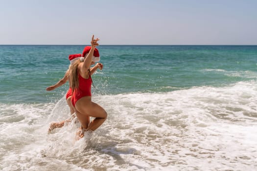 Women in Santa Claus hats run into the sea dressed in red swimsuits. Celebrating the New Year in a hot country.