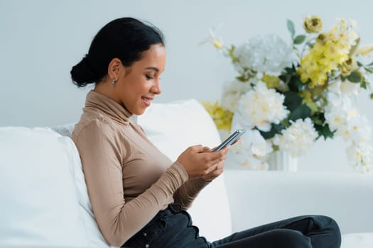 Relaxed young African American woman using crucial mobile phone on sofa couch in living room at home