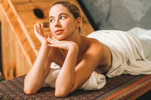 Pretty young woman lies on spa bed in front of wooden sauna cabinet. Attractive relaxing caucasian women in white towel waiting for body massage in spa salon, sauna room .Tranquility.