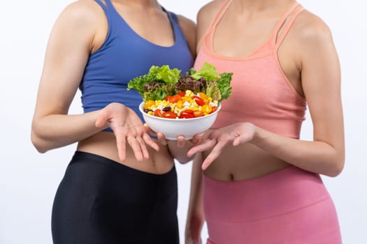 Two young sporty Asian women in sportswear holding salad bowl fill with fruit and vegetable. Natural youthful and fit body lifestyle people with balance nutrition on isolated background. Vigorous