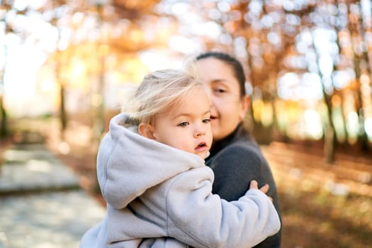 Little girl sits in her mother arms and looks away. High quality photo