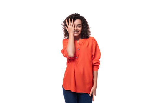 young curly brunette woman dressed in an orange blouse on a white background.