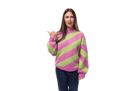 young caucasian woman with black hair dressed in a pink striped sweater points with her hand on a white background with space for advertising.