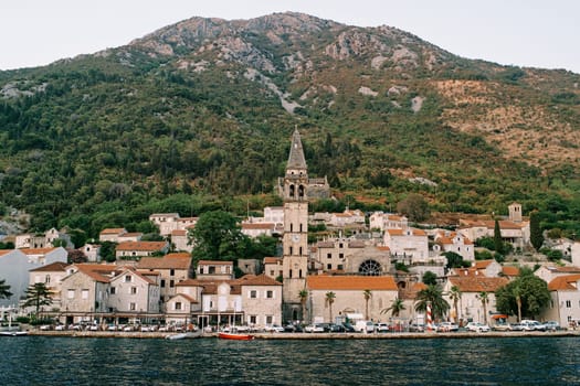 View from the sea of the bell tower of the Church of St. Nicholas among ancient houses at the foot of the mountains. Perast, Montenegro. High quality photo