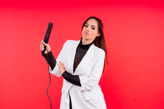 Happy young woman with beautiful hair holding curling iron on a grey and red background