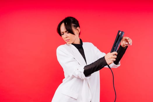 Happy young woman with beautiful hair holding curling iron on a grey and red background
