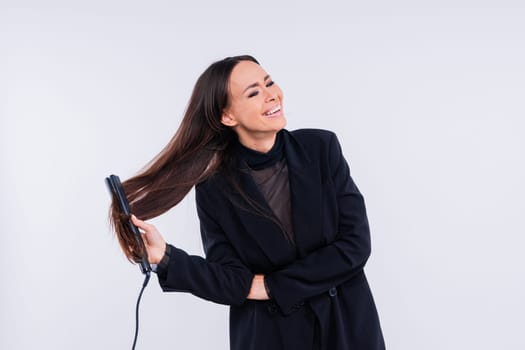 Happy young woman with beautiful hair holding curling iron on a grey and red background