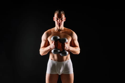 Man with pumped-up body with dumbbells in his hands white panties exercise