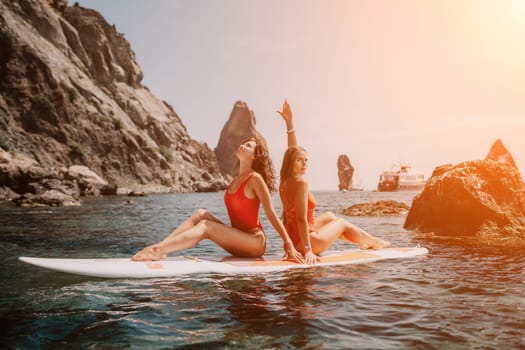 Woman sup yoga. Middle age sporty woman practising yoga pilates on paddle sup surfboard. Female stretching doing workout on sea water. Modern individual hipster outdoor summer sport activity