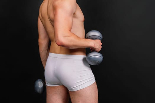 Man with pumped-up body with dumbbells in his hands white panties exercise
