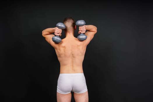Man with pumped-up body with dumbbells in his hands white panties exercise