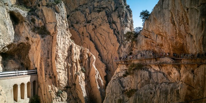 A train traverses tunnels while tourists stroll on Malaga's cliff pathways.