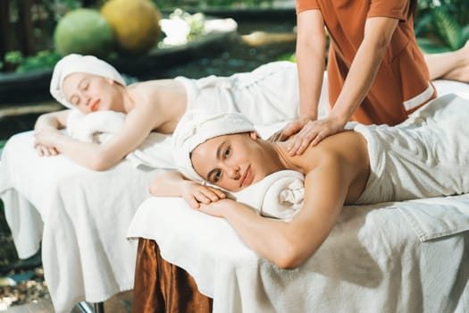 A portrait of two young attractive woman lie on bed during having back massage by a professional masseur at outdoor surrounded by peaceful natural environment. Healthy and beauty concept. Tranquility.