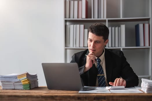 Unhappy young businessman feeling bored and stressed at work looking at laptop with hopeless expression while sitting in office.