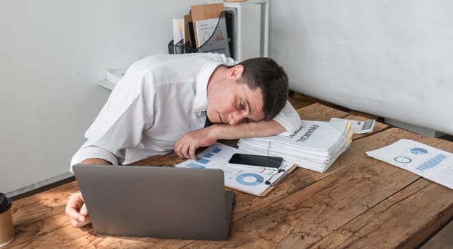 Unhappy young office worker feeling bored at work looking at laptop with a hopeless expression while sitting in the office. Male office worker feeling tired from monotonous work..