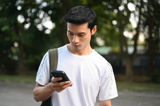 Attractive sporty man with backpack using mobile phone at a city park.