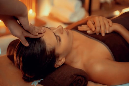 Caucasian woman enjoying relaxing anti-stress head massage and pampering facial beauty skin recreation leisure in warm candle lighting ambient salon spa in luxury resort or hotel. Quiescent