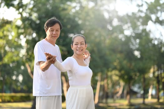 Active middle aged couple practicing Tai Chi Chuan in the park with sunrise. Mental health and wellbeing concept.