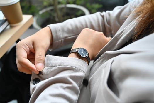Young businesswoman buttoning up a shirt sleeve and checking time on wrist watch for appointment.