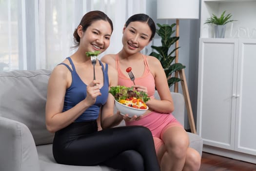 Young sporty Asian women in sportswear holding salad bowl together fill with vibrant of fruit and vegetable. Natural youthful and fit body lifestyle with balance nutrition and home exercise. Vigorous