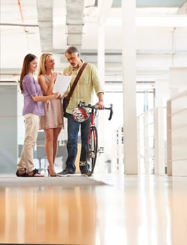 People, talking and document in office with bicycle for travel or morning commute to workplace. Bike messenger, paper and discussion of business, logistics or checklist with employees or clients.