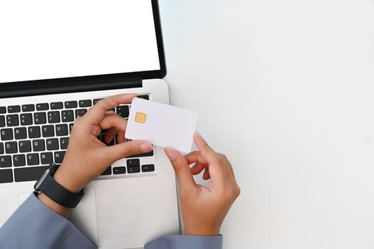 Above view of young woman holding credit card making purchase, payments on web stores via laptop.