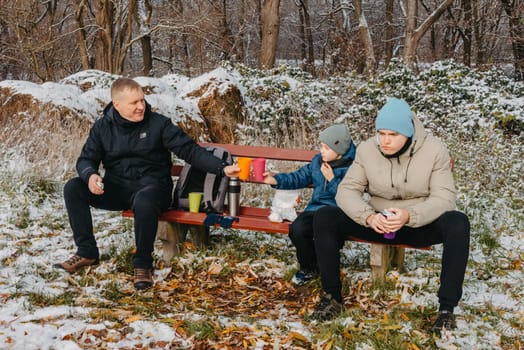 Snowy Park Serenity: Dad and Sons Share Treats and Smiles in a Winter Wonderland.