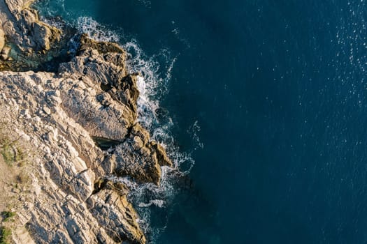 Clear blue sea rolls onto the high rocky shore. Top view. High quality photo