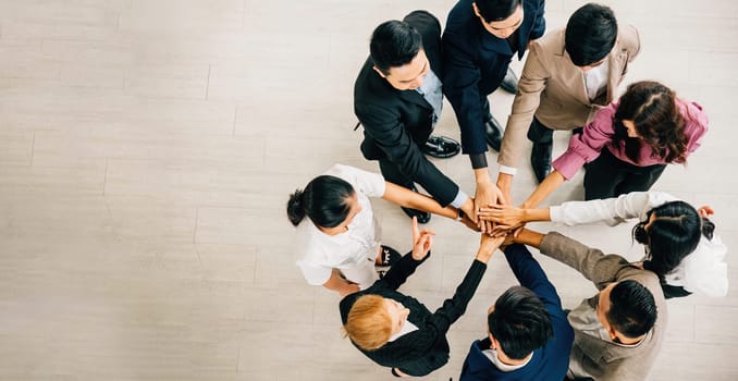 Four businesspeople of diverse backgrounds stand in a circle stacking their hands to represent unity. This image signifies teamwork success and global collaboration